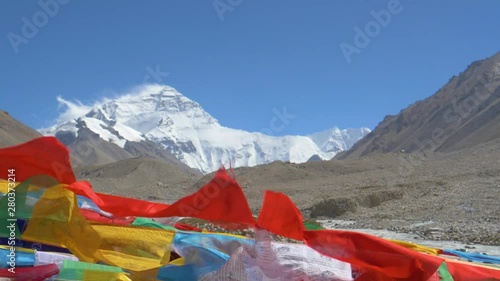 SLOW MOTION, CLOSE UP, DOF: Cinematic shot of buddhist flags flapping in front of snowy Everest. Winds blowing across Mount Everest Base Camp sweep ice and snow off the mountaintop and make flags flap