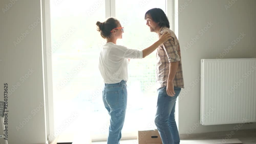 Happy newlyweds hugging standing by the window in a new apartment. Property rental, home purchase, loans for young families Happy newlyweds hugging standing by the window in a new apartment. Property rental, home purchase, loans for young families