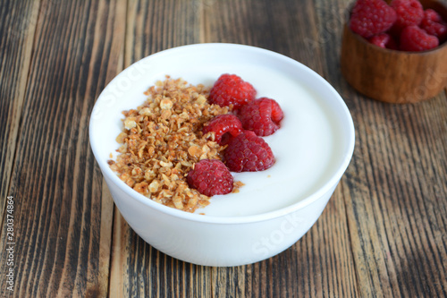 Delicious yogurt with granola and fresh raspberry in a bowl on wooden background Healthy food concept 
