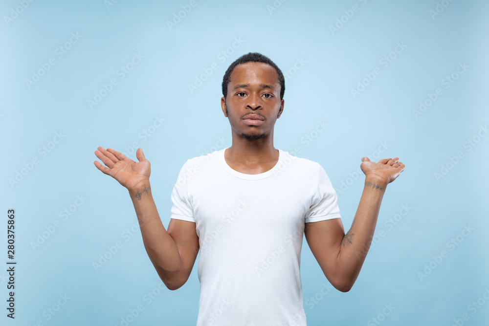 Half-length close up portrait of young african-american man in white shirt on blue background. Human emotions, facial expression, ad concept. Showing empty bar, pointing, choosing, inviting. Half-length close up portrait of young african-american man in white shirt on blue background. Human emotions, facial expression, ad concept. Showing empty bar, pointing, choosing, inviting.