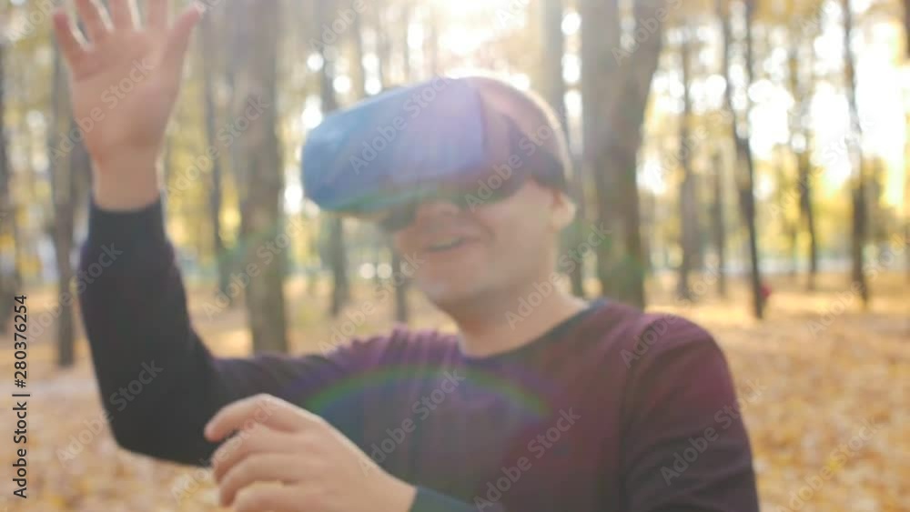 Guy in virtual reality headset is playing a game on sunny day in the autumn park Guy in virtual reality headset is playing a game on sunny day in the autumn park