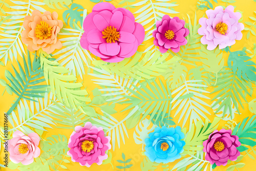 flat lay with paper cut multicolored flowers on tropical leaves on yellow bright background with copy space