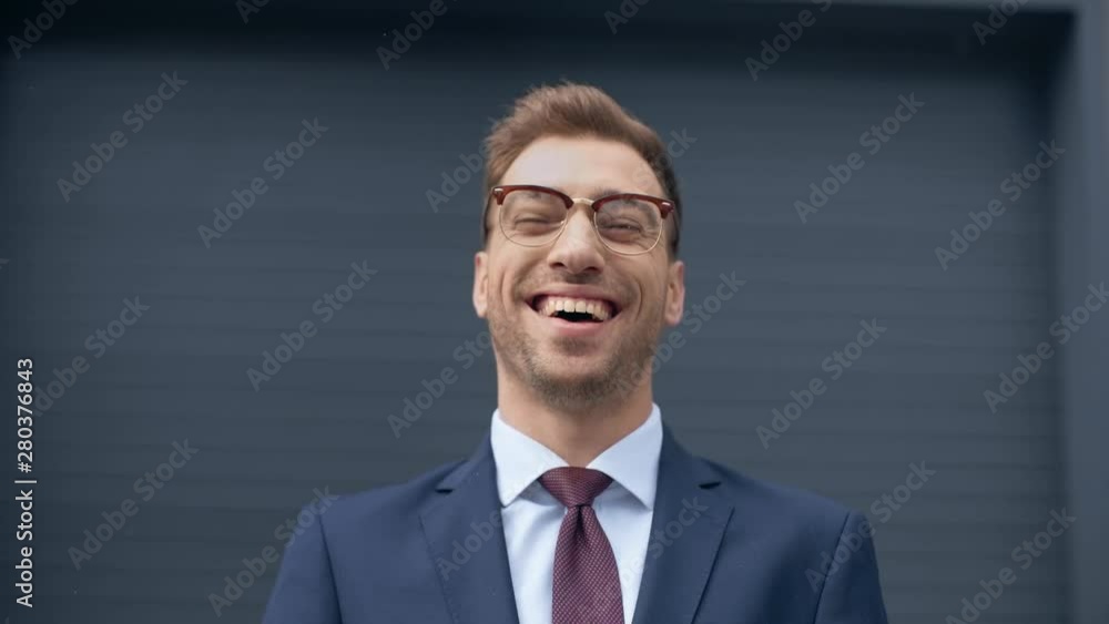 businessman in glasses looking at camera and laughing near grey wall businessman in glasses looking at camera and laughing near grey wall
