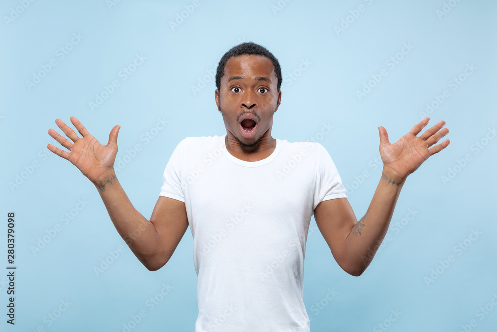 Half-length close up portrait of young african-american man in white shirt on blue background. Human emotions, facial expression, ad, sales concept. Inviting, looks shocked and astonished. Copyspace. Half-length close up portrait of young african-american man in white shirt on blue background. Human emotions, facial expression, ad, sales concept. Inviting, looks shocked and astonished. Copyspace.