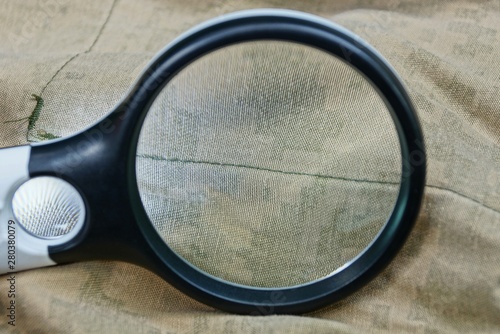 one black magnifier in the hand increases the brown green wrinkled fabric on the clothes 
