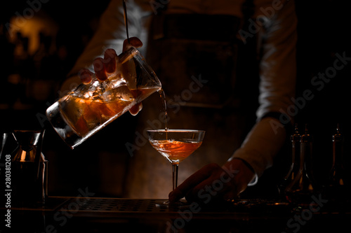 Bartender pouring the alcohol cocktail with strainer