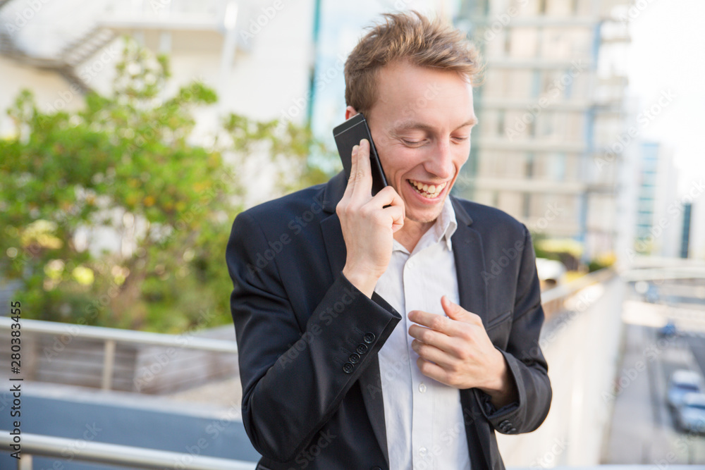 Excited joyful business man chatting on phone and getting good news outside. Happy cheerful manager talking on cellphone and laughing. Communication and good news concept Excited joyful business man chatting on phone and getting good news outside. Happy cheerful manager talking on cellphone and laughing. Communication and good news concept