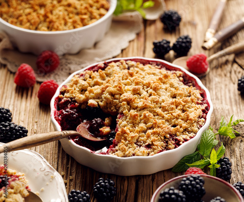 Crumble, Mixed berry (blackberry, raspberry) crumble, stewed fruits topped with crumble of oatmeal, almond flour, butter and sugar  in a baking dish on a wooden table, close-up photo