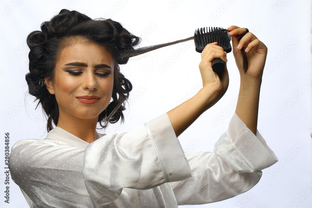 Morning preparation. The girl is combing her hair. Sad young girl wanted to make a beautiful hairstyle with the help of curlers, but loses her hair. Beautiful girl in hair curlers isolated on white. Morning preparation. The girl is combing her hair. Sad young girl wanted to make a beautiful hairstyle with the help of curlers, but loses her hair. Beautiful girl in hair curlers isolated on white.
