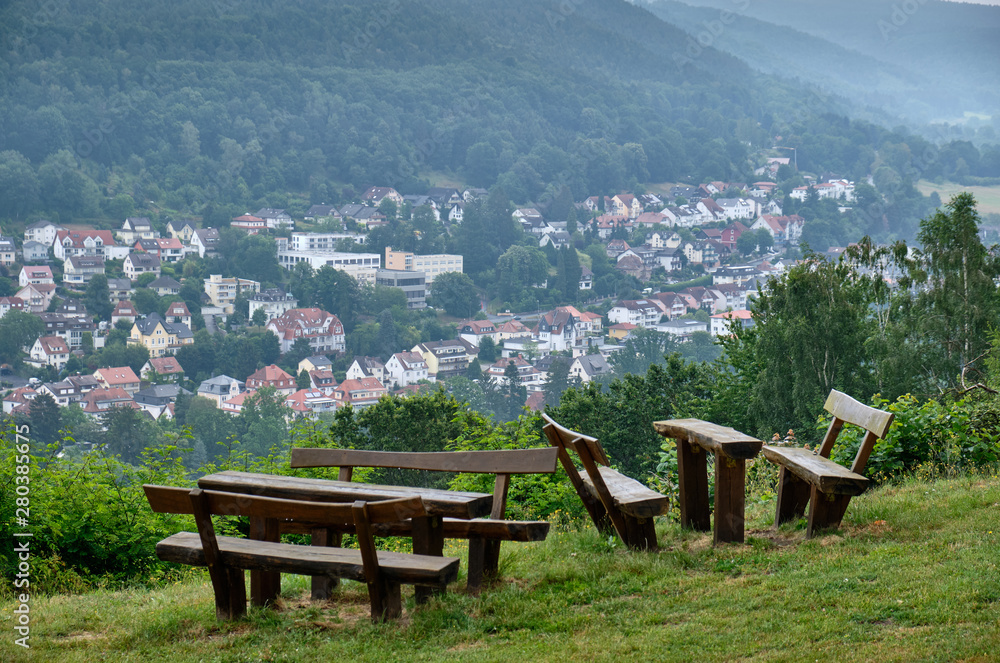Bad Orb, Germany - July 13, 2019: A view from the Mollkenberg hill in the Spessart on the townscape of Bad Orb with empty benches and tables in the foreground Bad Orb, Germany - July 13, 2019: A view from the Mollkenberg hill in the Spessart on the townscape of Bad Orb with empty benches and tables in the foreground