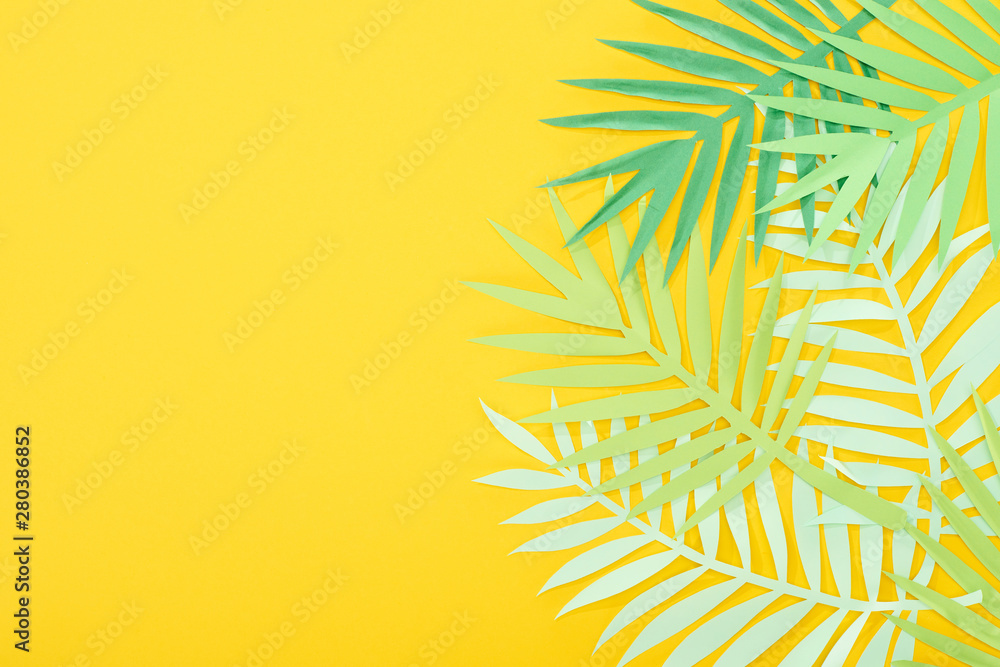 top view of paper cut green tropical leaves on yellow bright background with copy space