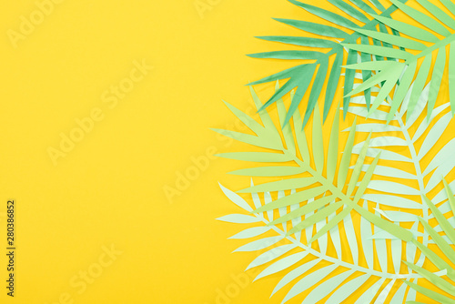 top view of paper cut green tropical leaves on yellow bright background with copy space