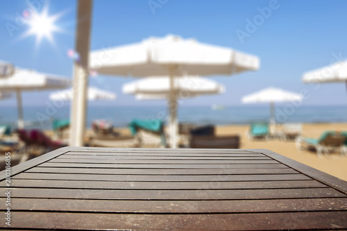 Table background with beautiful blue ocean and sandy beach view. A table with sunbeds and umbrellas and the sea in distance. Summer sunny day. © magdal3na
