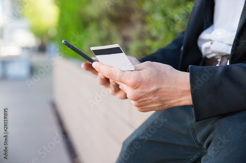 Closeup of credit card and phone in human hands. Man in office suit using smartphone and credit card for online payment. Online money transfer concept
