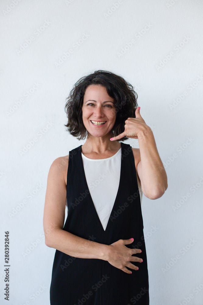 Happy woman asking for call. Cheerful middle aged woman with curly hair showing call me gesture and smiling at camera. Communication concept Happy woman asking for call. Cheerful middle aged woman with curly hair showing call me gesture and smiling at camera. Communication concept