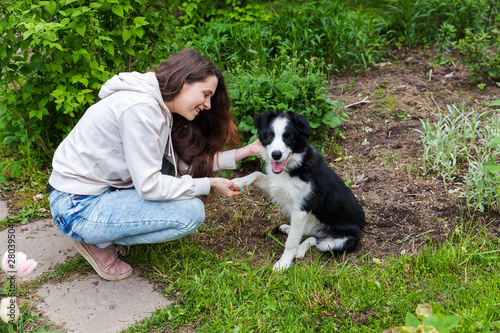 Smiling young attractive woman embracing cute puppy dog border collie in summer city park outdoor background. Girl huging new lovely member of family. Pet care and animals concept