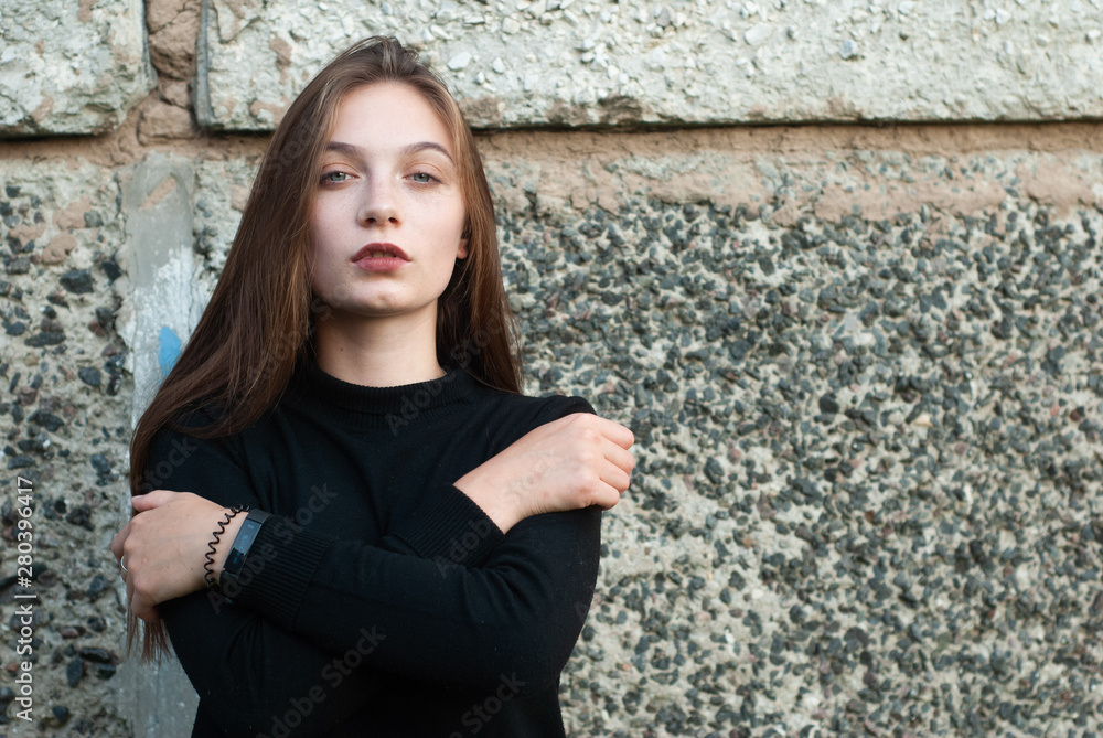 Beautiful young girl in a black turtleneck sweater posing in the concrete wall,