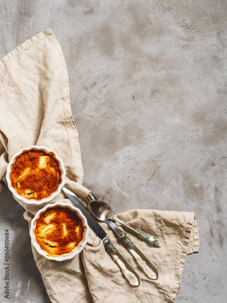 Fototapeta premium Flat lay of prepared apple cakes, tarts, puddings in a porcelain baking dish on a gray concrete background with a linen napkin and space for the recipe text