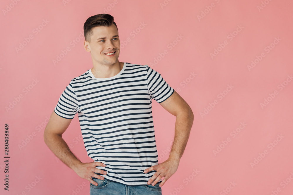 smiling young man in striped t-shirt with hands on hips isolated on pink smiling young man in striped t-shirt with hands on hips isolated on pink