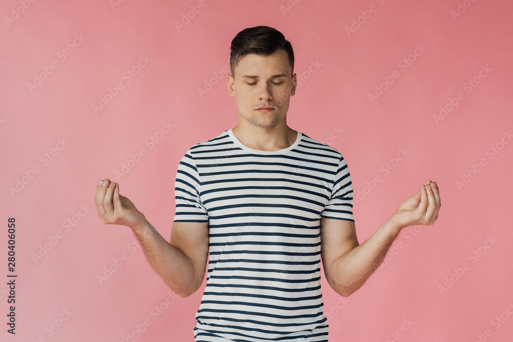 front view of relaxed young man in striped t-shirt meditating with closed eyes isolated on pink front view of relaxed young man in striped t-shirt meditating with closed eyes isolated on pink