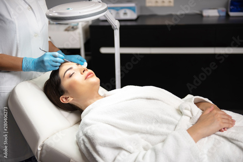 Cosmetologist using blackhead remover for cleaning lady face in spa salon