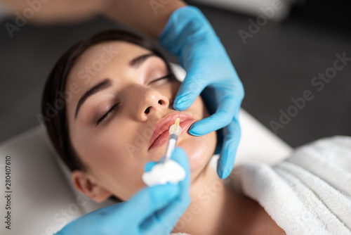 Beautician in sterile gloves making injection in lady lips