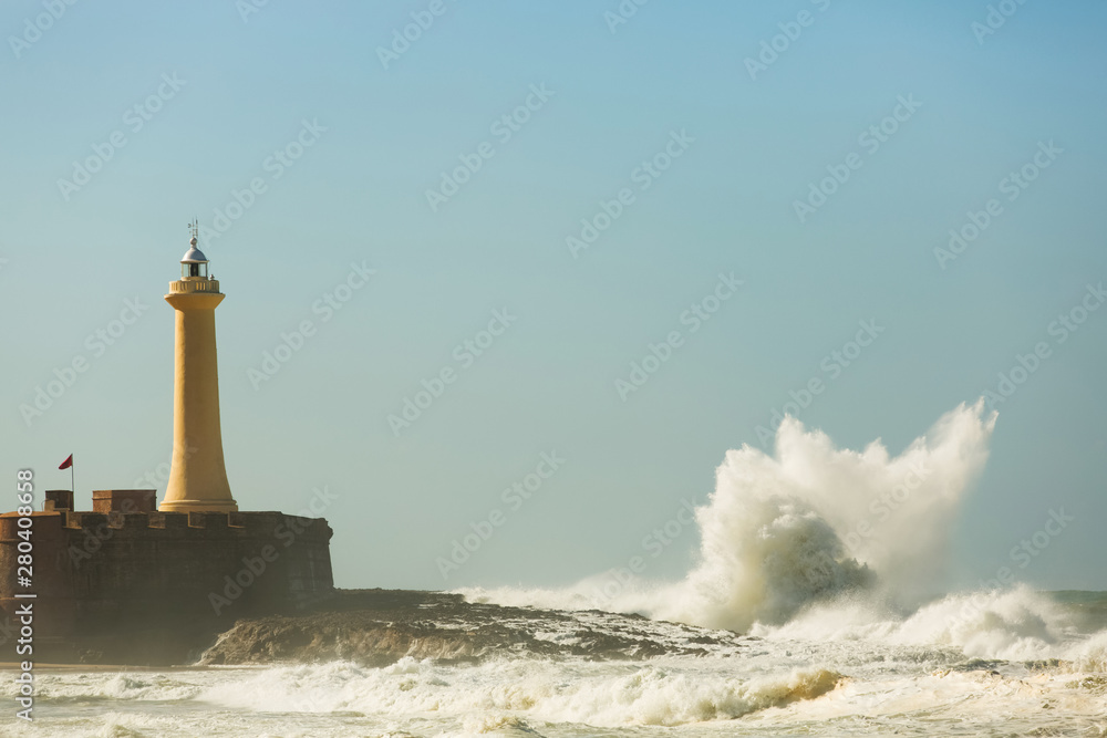 Crashing waves at the lighthouse in sunny weather on a blue sky background