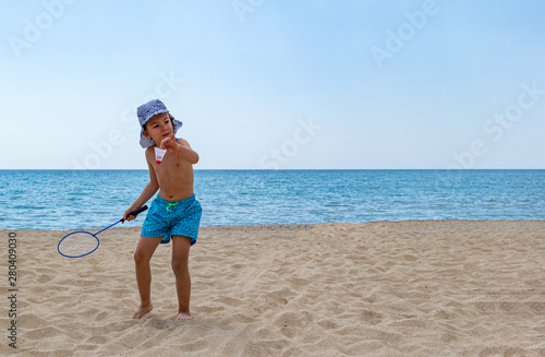 The child plays with a badminton racket and a shuttlecock on the beach. The concept of a family holiday. Copy space.