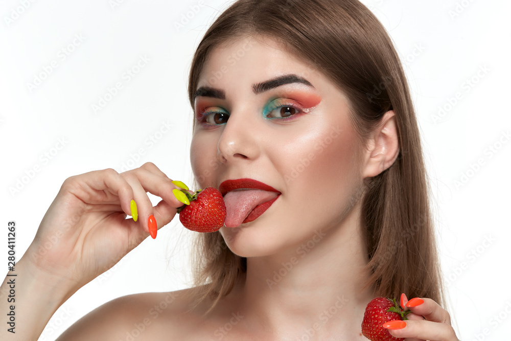Closeup portrait of a beautiful young woman with bright color make-up holding strawberry near the face. Closeup portrait of a beautiful young woman with bright color make-up holding strawberry near the face.