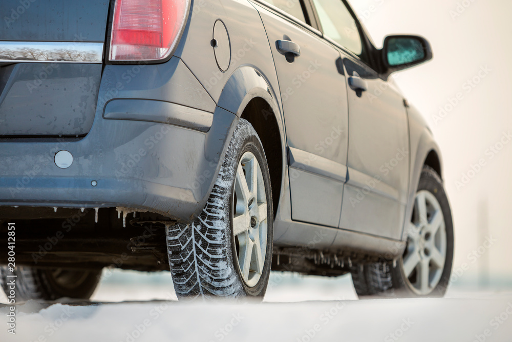 Close up of a car tire parked on snowy road on winter day. Transportation and safety concept.
