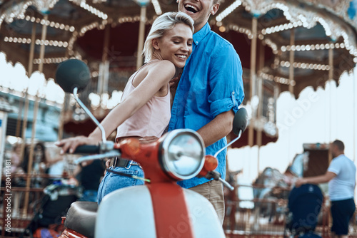 Two people with motorbike laughing near the merry-go-round