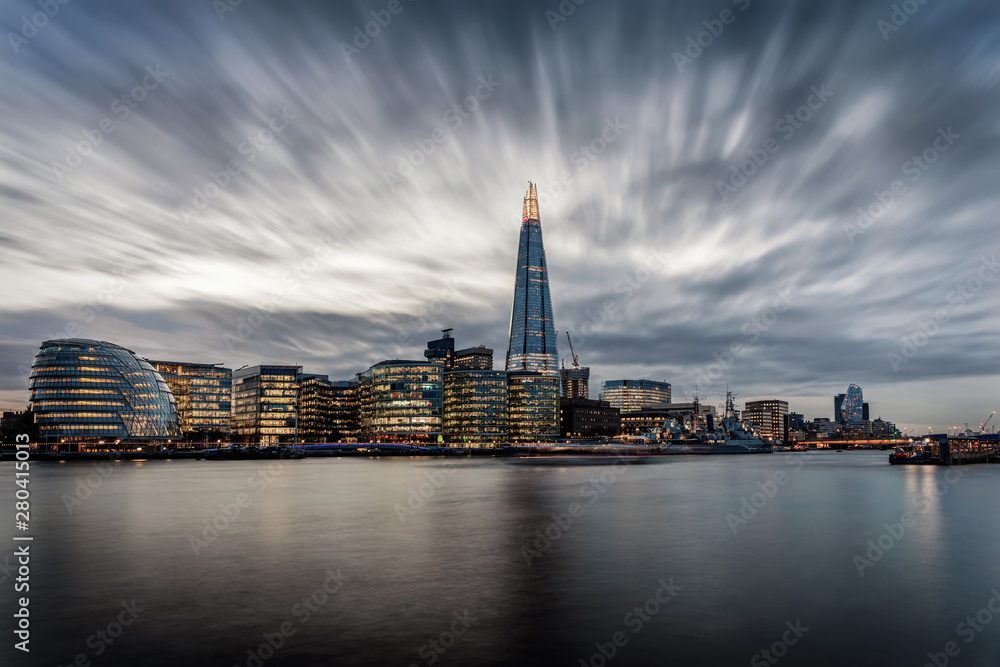 Die markante Skyline von London an der Themse mit den beleuchteten Wolkenkratzern am Abend mit Wolken, Großbritannien
