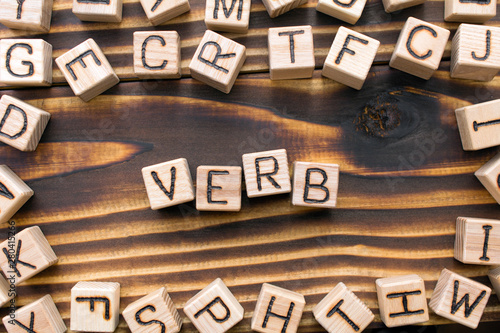 word verb composed of wooden cubes with letters, Part of speech concept scattered around the cubes random letters, top view on wooden background photo