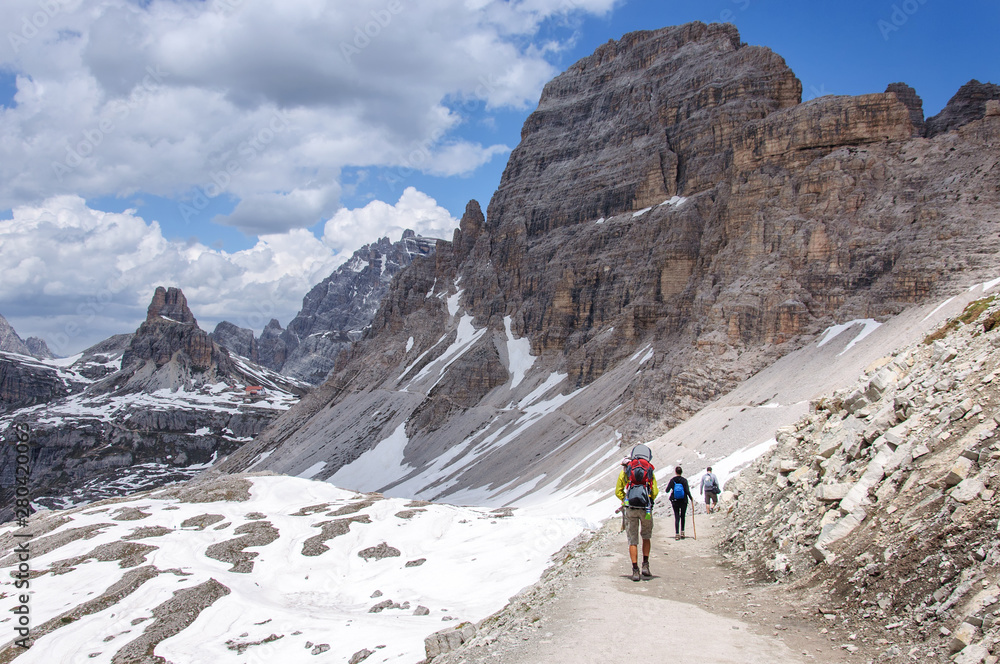 a group of tourists is walking along a wide trail in the Dolomites, Italy