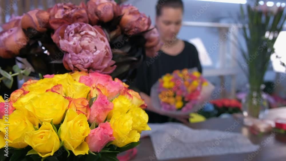 Floral business concept. Blur background with professional florist woman packaging roses boquet in flower shop. White and pink roses and peonies on table in vases. Working in floristic studio store. Floral business concept. Blur background with professional florist woman packaging roses boquet in flower shop. White and pink roses and peonies on table in vases. Working in floristic studio store.