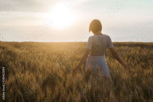 Middle age woman in a dress on a wheat field at sunset. Freedom, naturalness, nature concept.