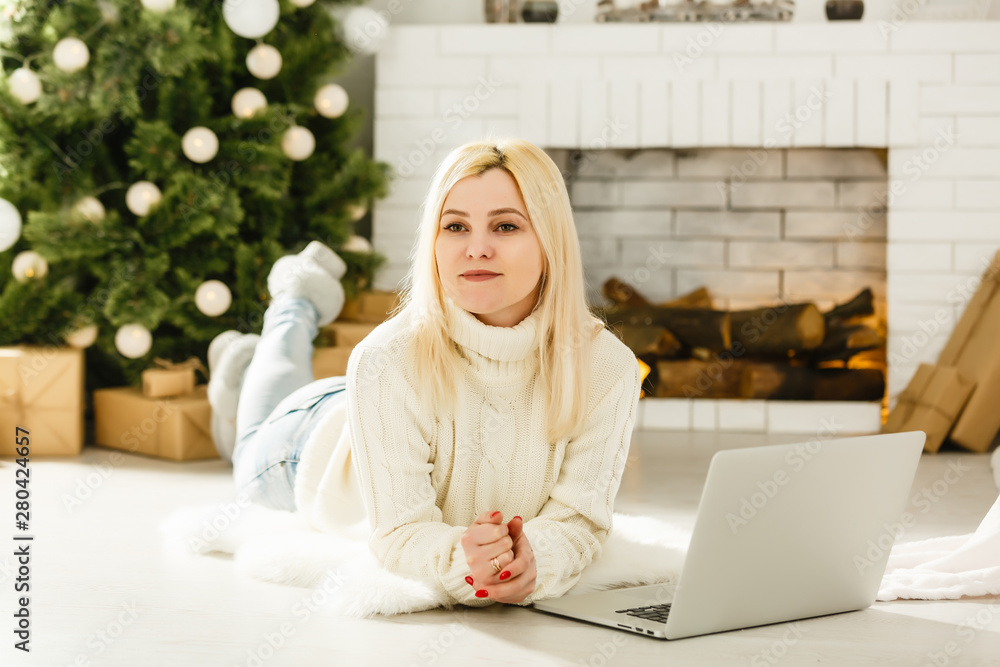 Young woman shopping online on laptop in cozy christmas interior. Girl in casual sitting under pine tree among lots of beautifully wrapped presents. Prepare to xmas, bying on winter sales. Copy space Young woman shopping online on laptop in cozy christmas interior. Girl in casual sitting under pine tree among lots of beautifully wrapped presents. Prepare to xmas, bying on winter sales. Copy space