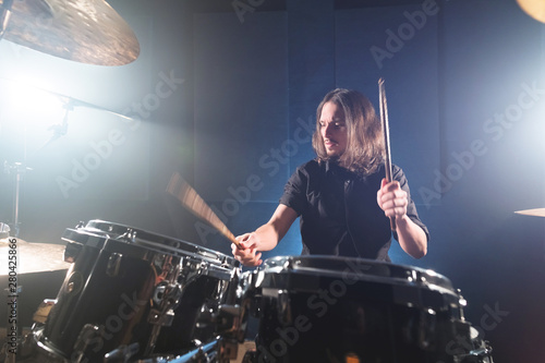 Portrait of a long-haired drummer with chopsticks in his hands sitting behind a drum set. Low key. Concepts of the creative freedom of the millenial generation