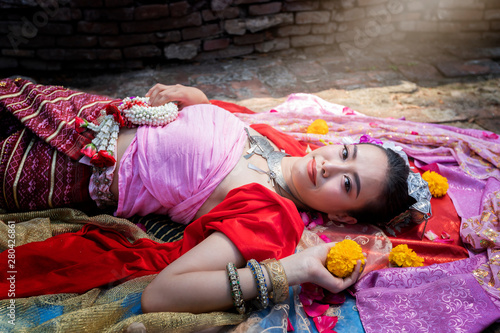 Beautiful Thai woman wearing thai traditional clothing lie down on silk of various colors. © skarie