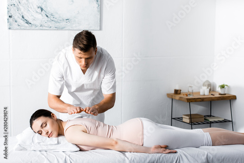 focused healer standing near woman lying on massage table with closed eyes and holding hands above her body