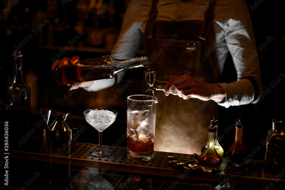Bartender prepares alcohol cocktail using jigger with handle