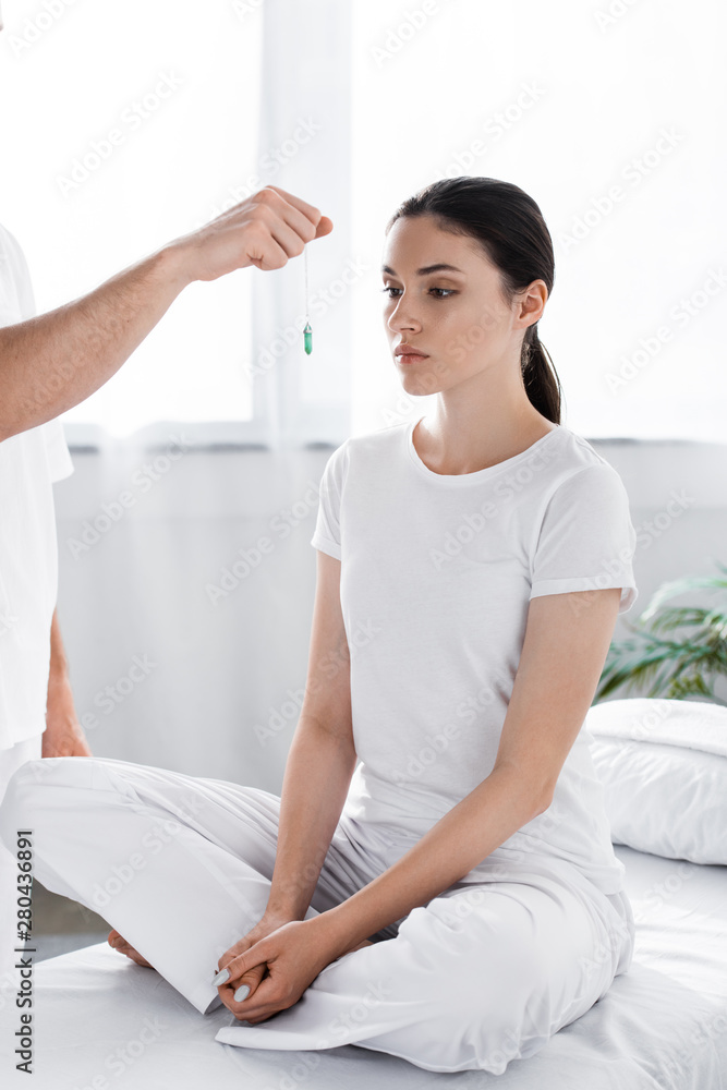 cropped view of hypnotist standing near woman and holding green stone near her face