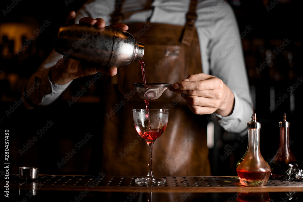 Bartender flowing cocktail through sieve in glass