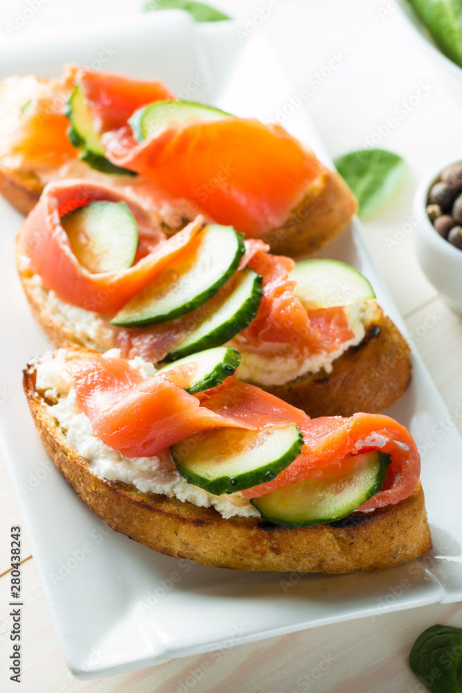 Salmon, cucumber and cream cheese bruschetta. Italian tapas, antipasti with vegetables, herbs and oil on grilled ciabatta and baguette bread. Sandwich.