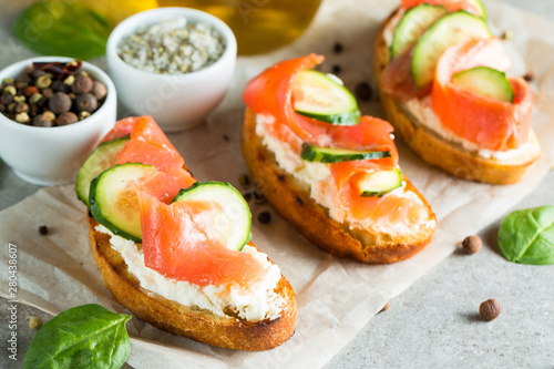 Salmon, cucumber and cream cheese bruschetta. Italian tapas, antipasti with vegetables, herbs and oil on grilled ciabatta and baguette bread. Sandwich.