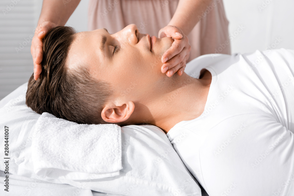 cropped view of masseur standing near man with closed eyes and touching his face cropped view of masseur standing near man with closed eyes and touching his face