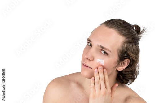 Handsome young shirtless man applying cream at his face on white background isolated. Men health and skin care