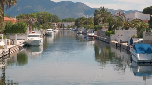 Amazing view on marine canal with boats and houses. Mooring of yachts near the house. Resort cityscape, palm trees, little Spanish Venice, Empuriabrava. Rich lifestyle. Summer, mountains, scenic view.