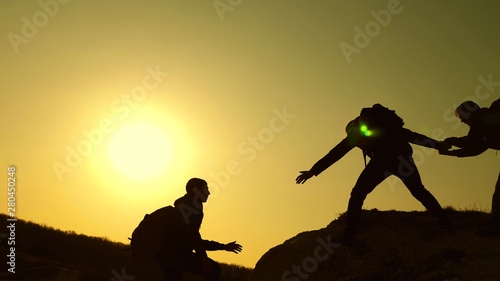 teamwork of business people. travelers climb one after another on rock. joint business. Slow motion. Climbers silhouettes stretch their hands to each other, climbing to top of hill. sport climber.