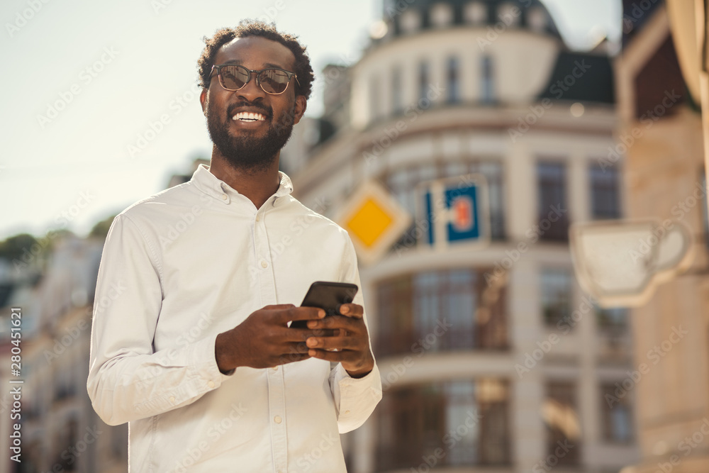 Joyful man looking up while standing with smartphone